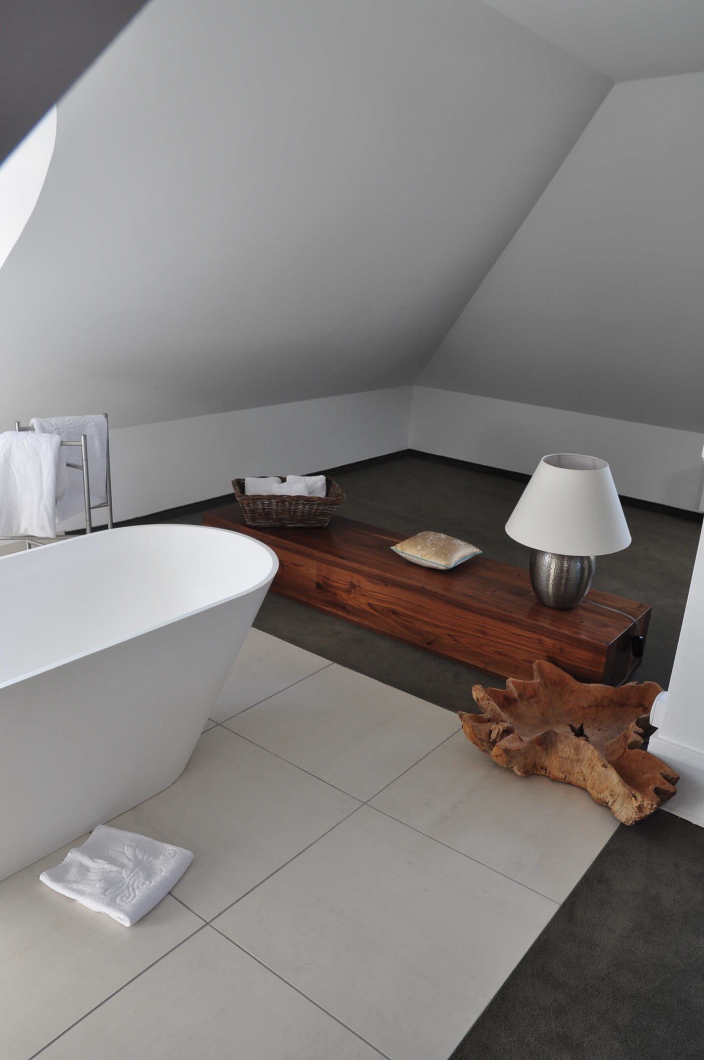 Un baño moderno con una bañera independiente, un tocador de madera, una lámpara y una piedra decorativa.