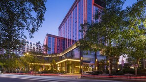 Un hotel moderno con fachada de vidrio, entrada curva e iluminación roja en el exterior.