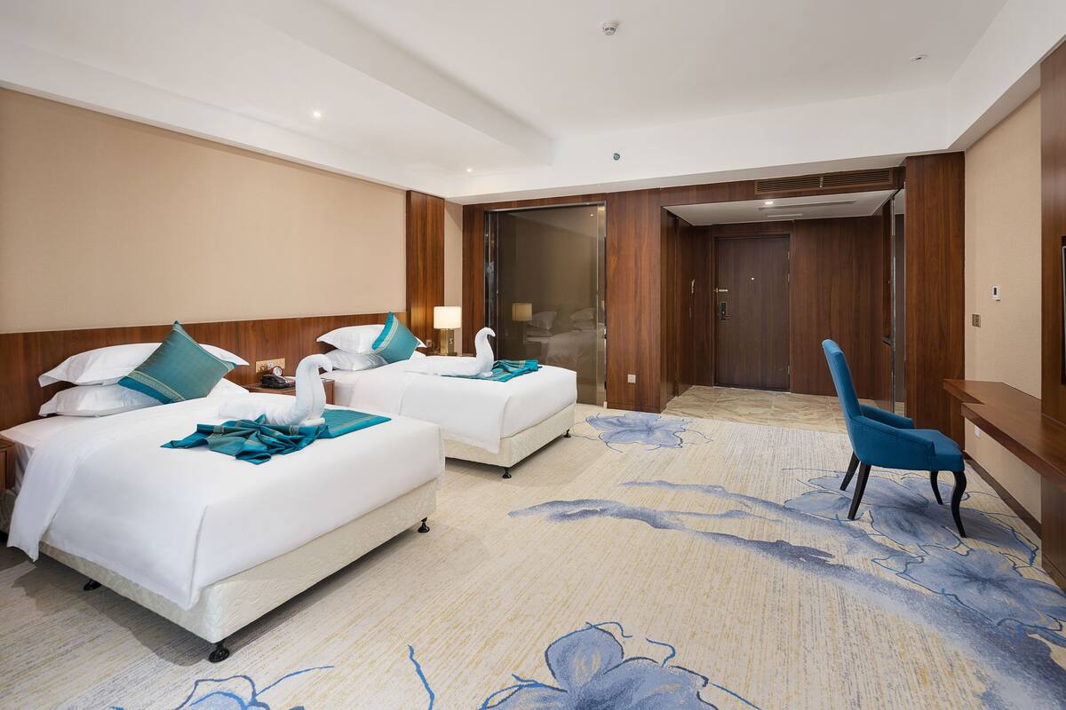 Habitación de hotel con dos camas, una silla azul y un ventanal grande.