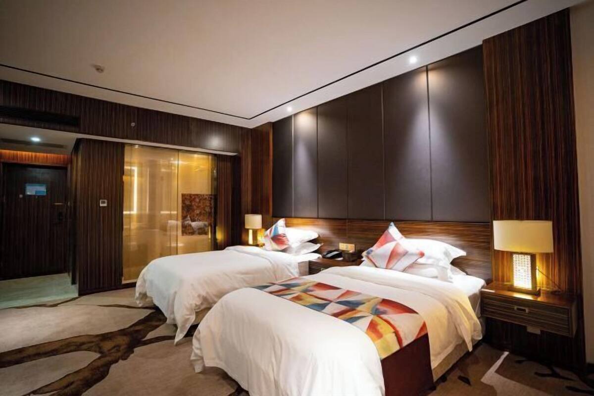 Una habitación de hotel con dos camas, un espejo grande y un panel de pared de madera.
