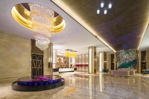 A spacious lobby with a large chandelier, a round seating area, and a large wall mural. - Headquarter International Hotel (Guangzhou)