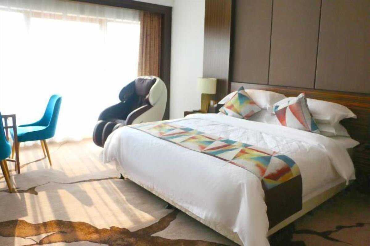 Una habitación de hotel con cama, una silla, una lámpara y vistas al exterior.