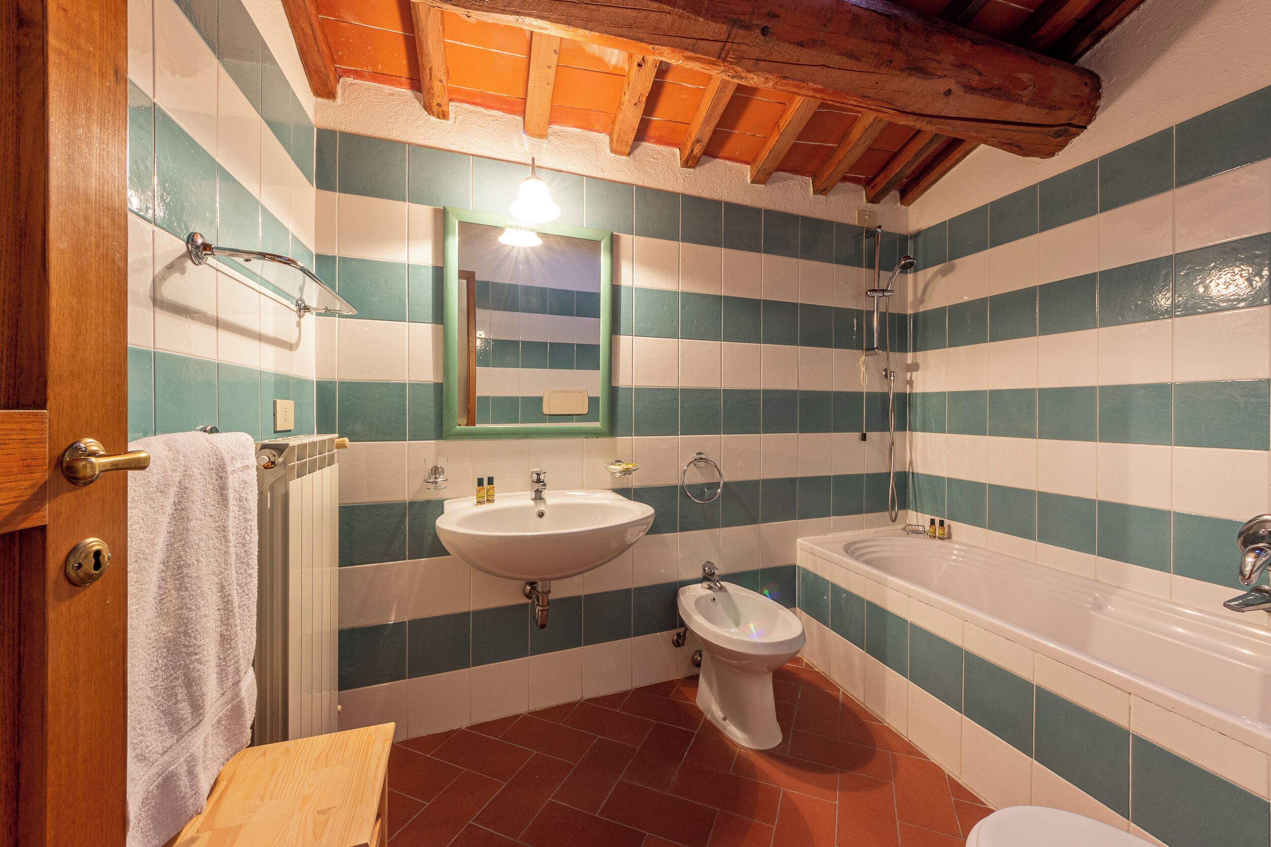 A bathroom with striped tile walls, a sink, a bidet, a toilet, and a wooden ceiling.