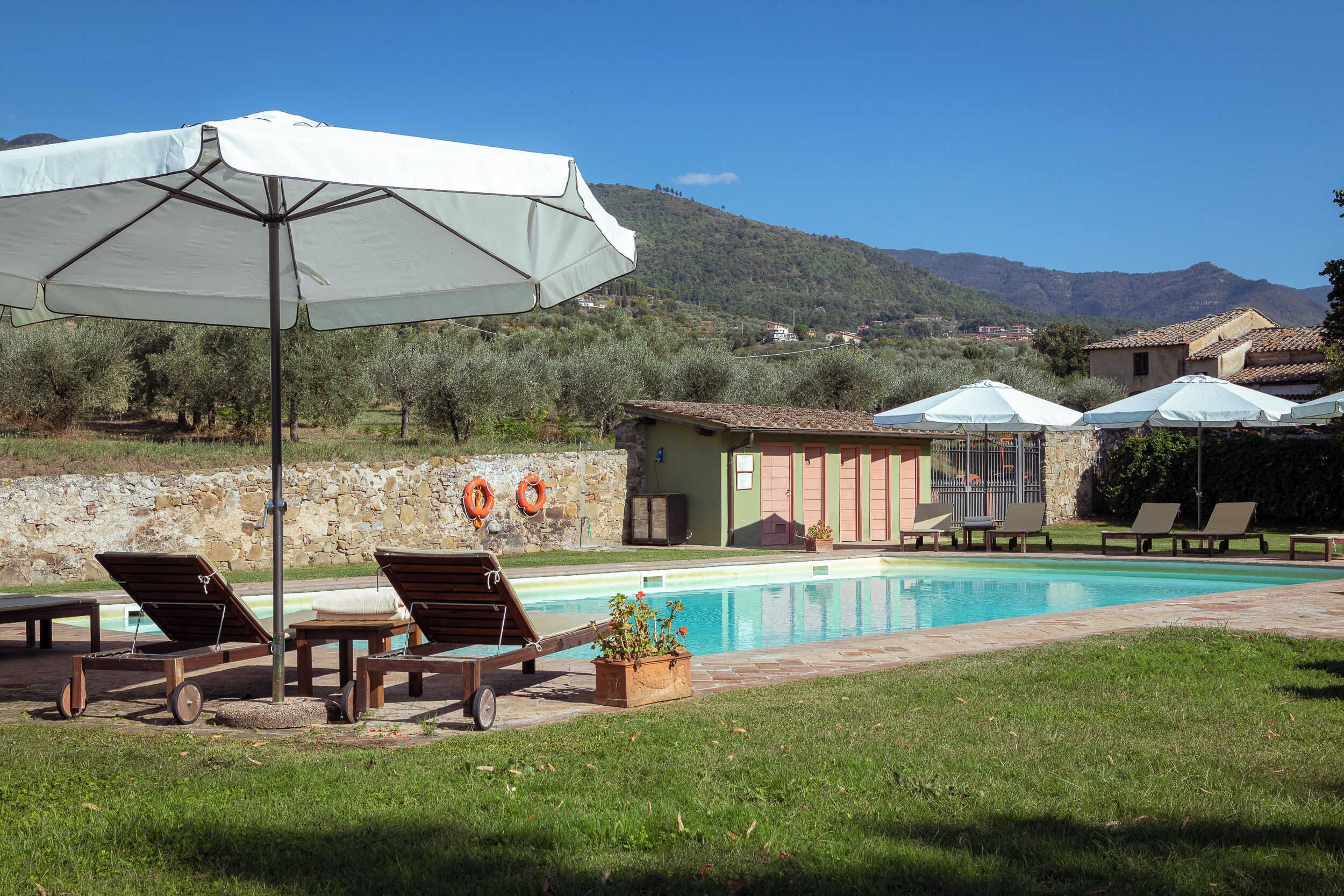 Un área junto a la piscina con sillones de descanso, sombrillas y una pared de piedra.