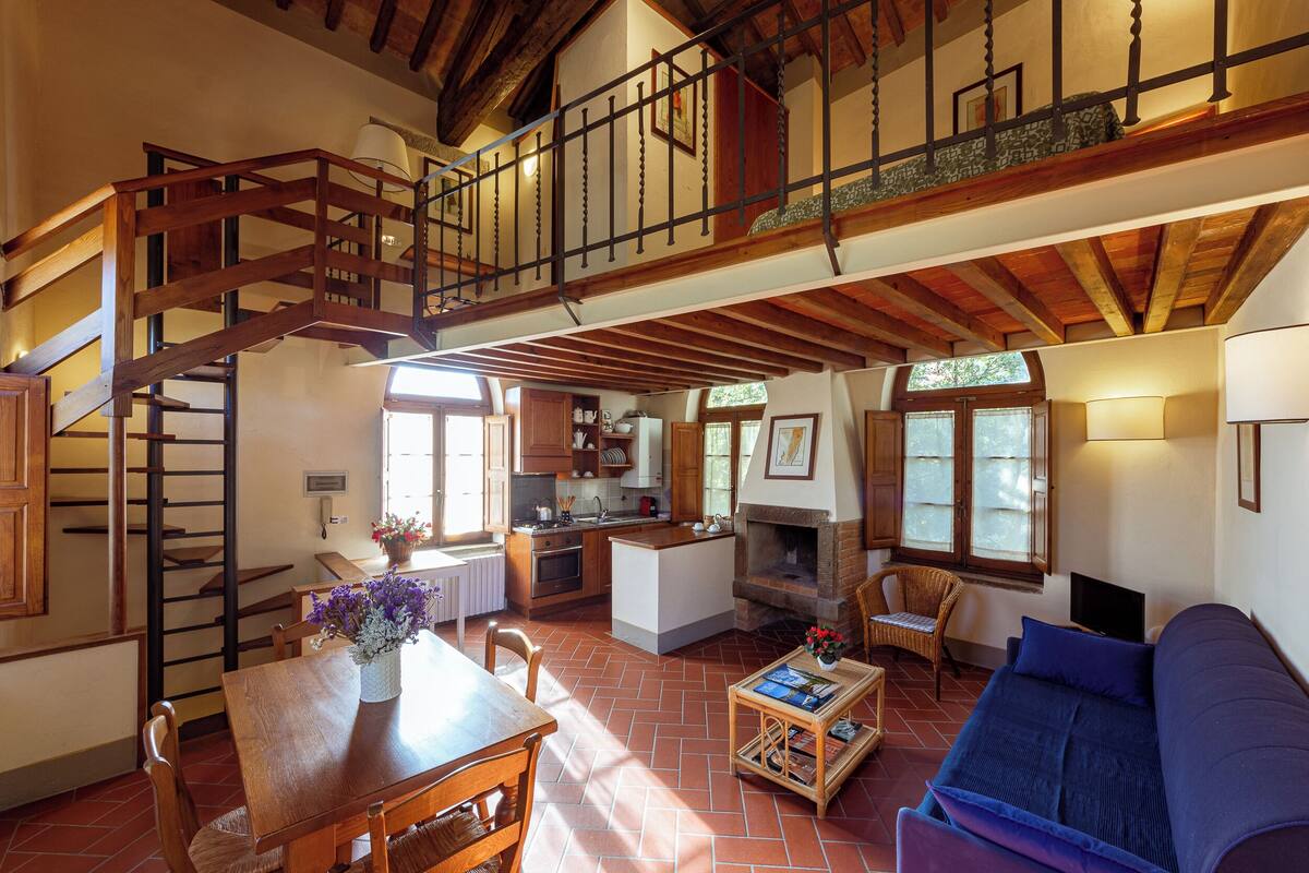 Uma sala de estar ampla com escada de madeira, lareira, mesa de jantar e sofá.