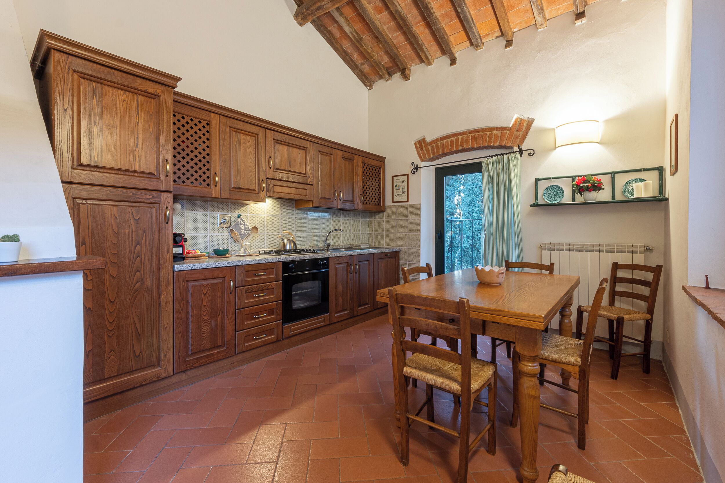 A kitchen with wooden cabinets, a dining table with chairs, and a brick ceiling.