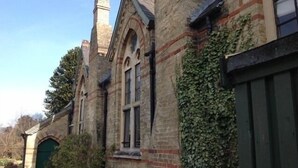A historic building with arched windows and a brick facade, featuring a green door and ivy-covered walls. - Chalk And Cheese (King's Lynn)