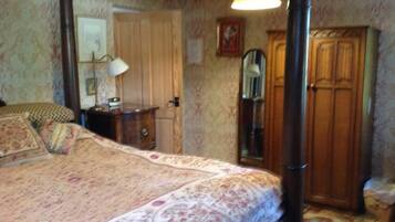 A bedroom with a four-poster bed, a wooden wardrobe, a mirror, and a lamp.