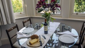 Una mesa redonda de vidrio con platos blancos, una botella de vino y un pan.