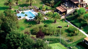 Eine Vogelperspektive auf ein Resort mit Schwimmbad, Tennisplätzen und üppigem Grün.