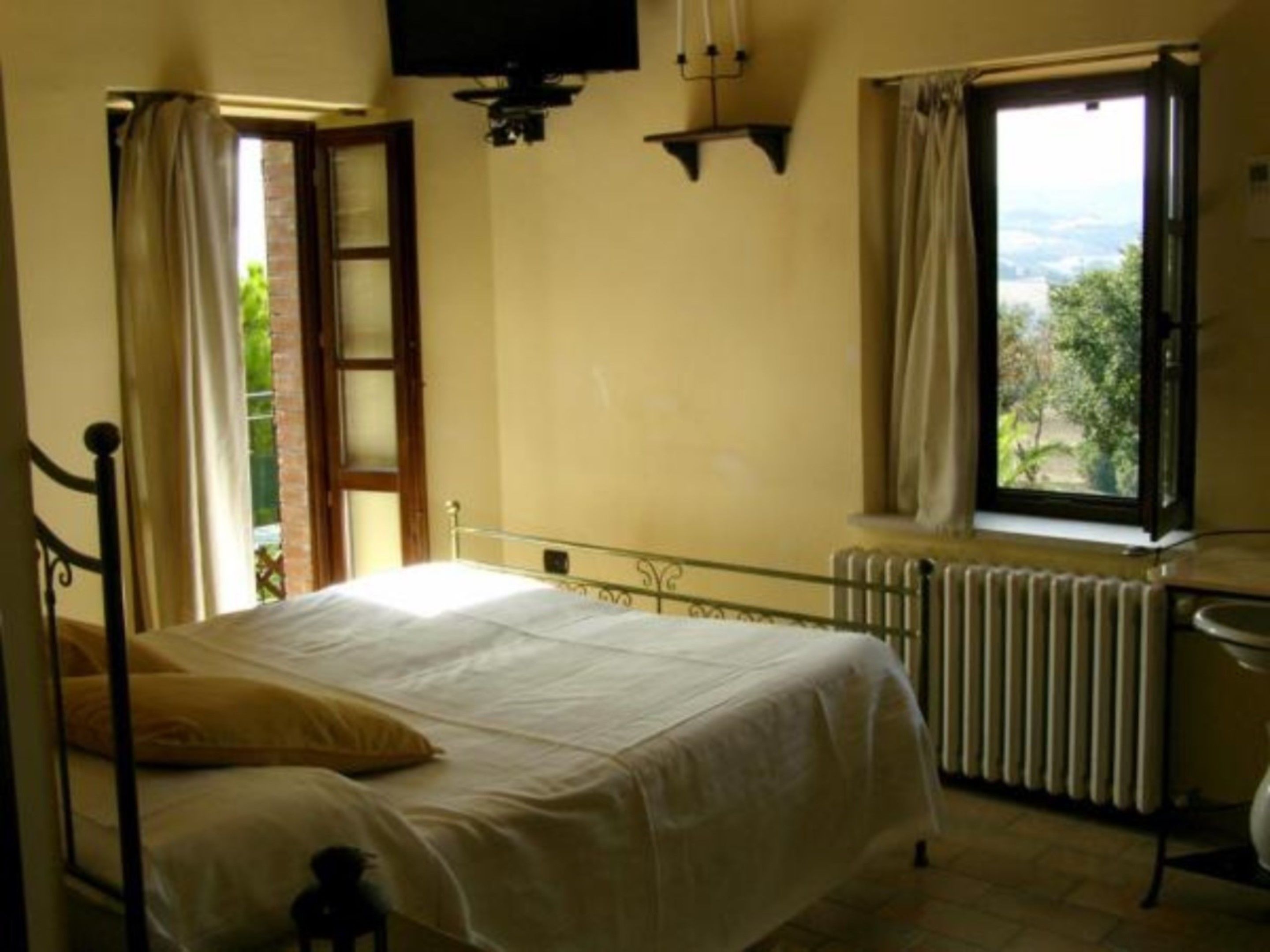 Une chambre à coucher avec un lit, une fenêtre avec des rideaux, un radiateur et un téléviseur fixé au mur.