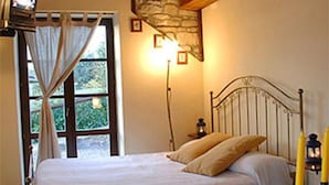 Ein Schlafzimmer mit einem Bett, einer Steinwand, einem Fenster mit Vorhängen, einem Fernseher und einer Wandleuchte.