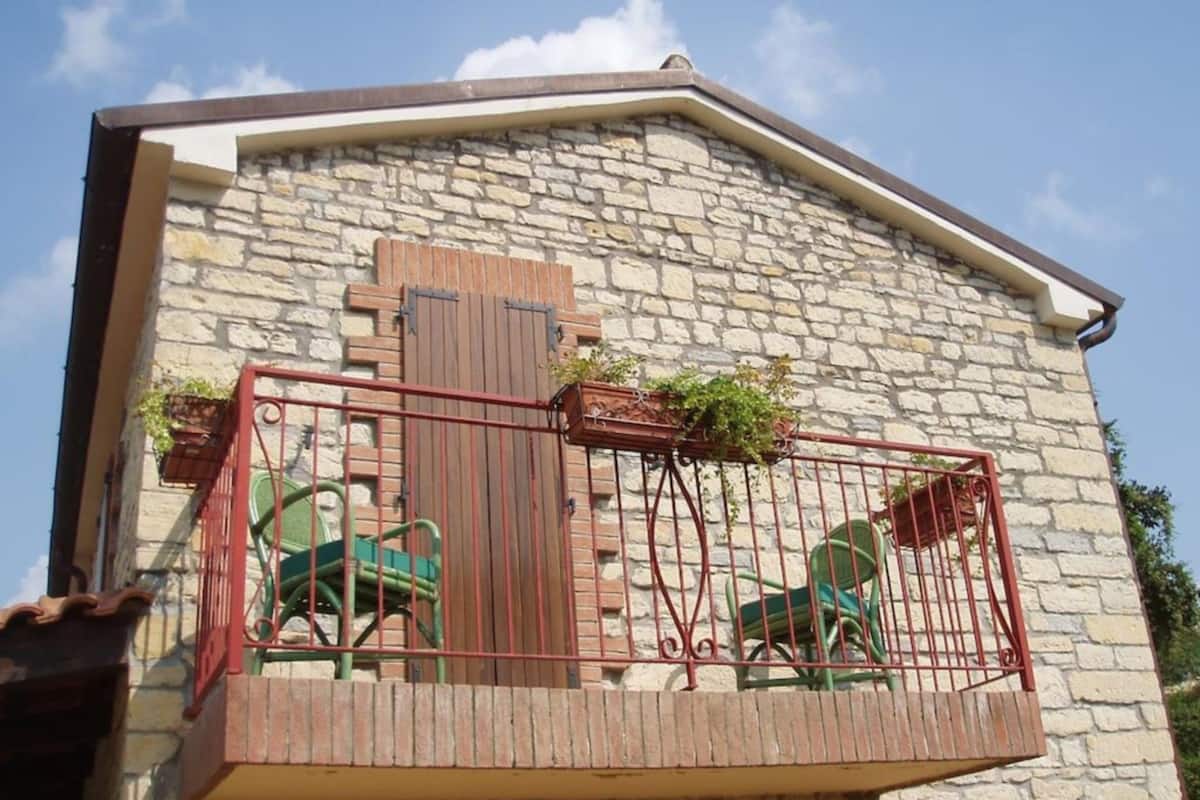 Ein Steinhaus mit einem Balkon, der mit Metallgeländern und zwei grünen Stühlen ausgestattet ist.