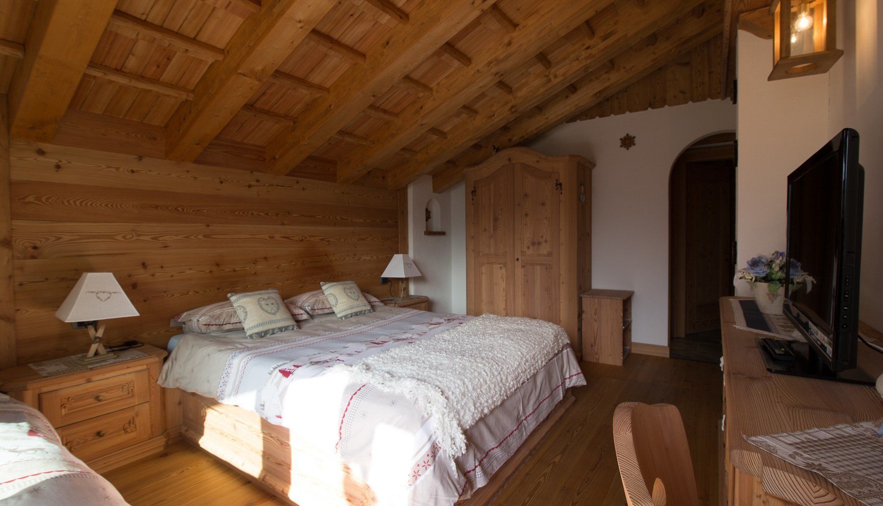 Ein gemütliches Zimmer aus Holz mit einem Bett, Nachttischen, einem Schreibtisch und einem Fernseher.