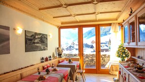 Un comedor con mesas dispuestas para dos, bancos de madera y vistas a un pueblo nevado a través de amplios ventanales.