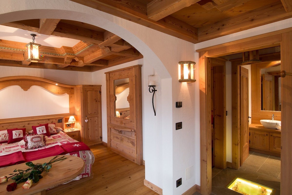 Un dormitorio acogedor con techo de madera, una cama grande con ropa de cama roja y una puerta de madera que da a un baño.