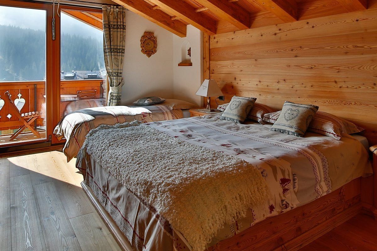 Acogedor dormitorio de cabaña de madera con una cama grande, una mesita de noche pequeña y una ventana con vistas a un paisaje nevado.