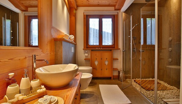 Un baño con un lavamanos de diseño, armarios de madera, un inodoro y una ducha con mampara de vidrio.