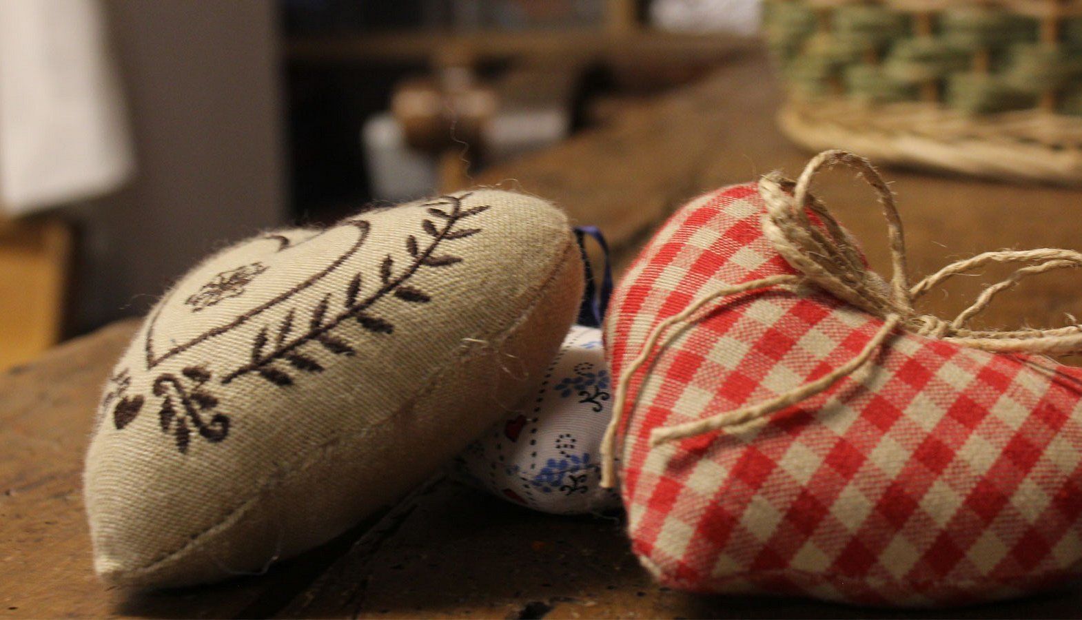 Deux petits objets en tissu, cousus à la main, l’un orné d’un motif de feuilles et l’autre d’un motif à carreaux, sont posés sur une surface en bois.