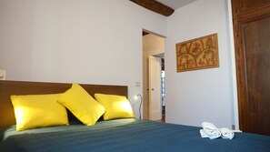 Una cama con almohadas amarillas, una colcha azul y una toalla doblada al lado.