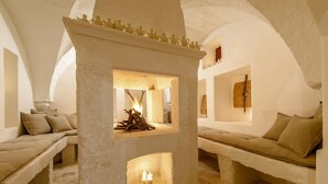 A cozy, rustic interior with a central stone fireplace, benches, and a small shelf with candles. - Masseria Stefanodelconte (Fasano)