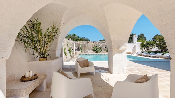 A sunlit outdoor seating area with white chairs and a table, overlooking a pool and a rocky landscape. - Masseria Stefanodelconte (Fasano)