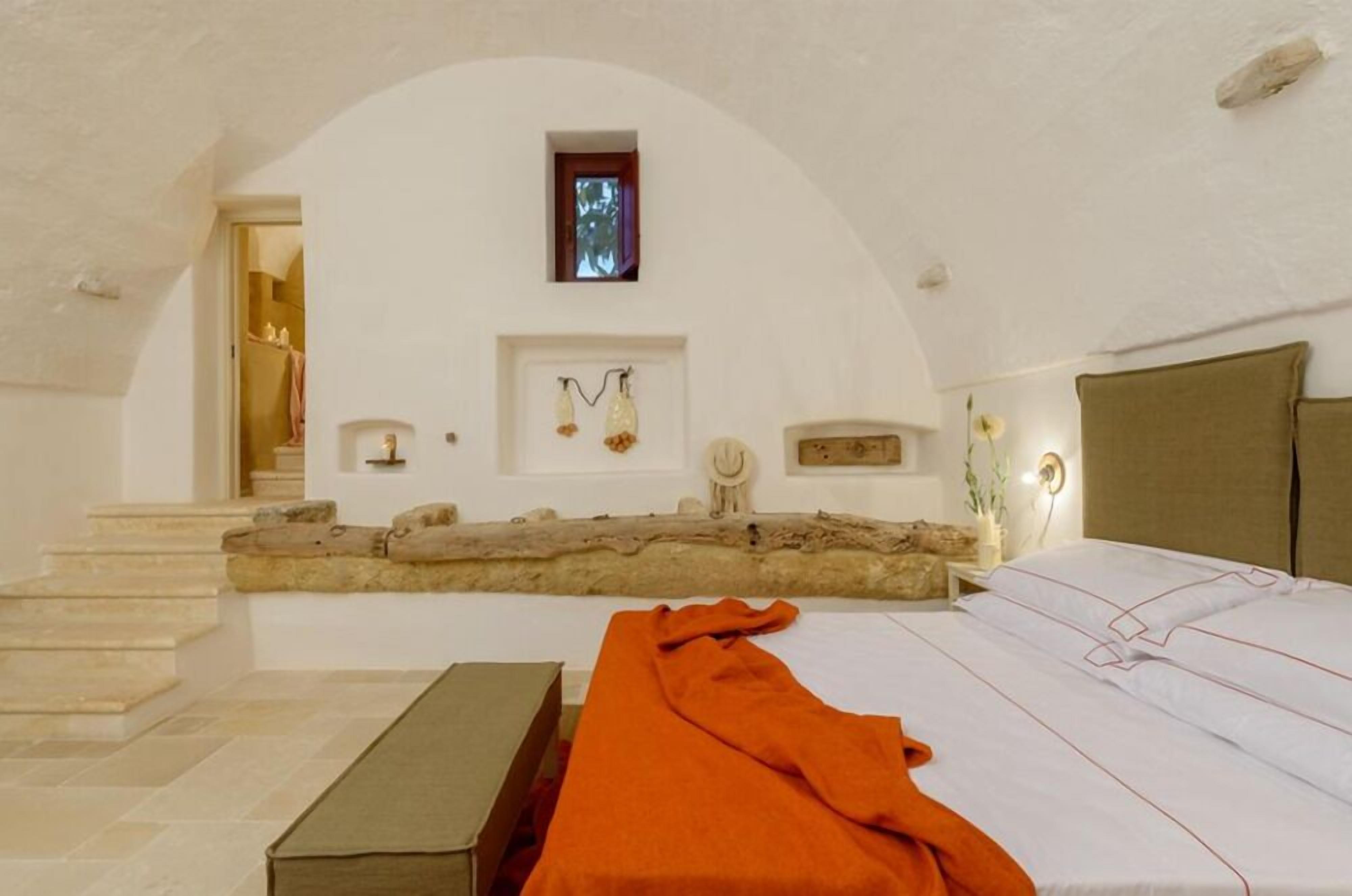 A bedroom with a bed, a bench, a stone ledge, and a small window.