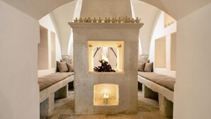 A stone fireplace with a fire, flanked by two benches with cushions. - Masseria Stefanodelconte (Fasano)