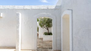 A white-walled courtyard with a tiled floor, an arched doorway, and a tree in the background. - Masseria Stefanodelconte (Fasano)