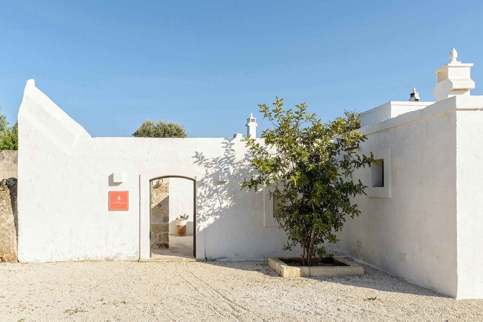 A white building with a door and a small tree in front.
