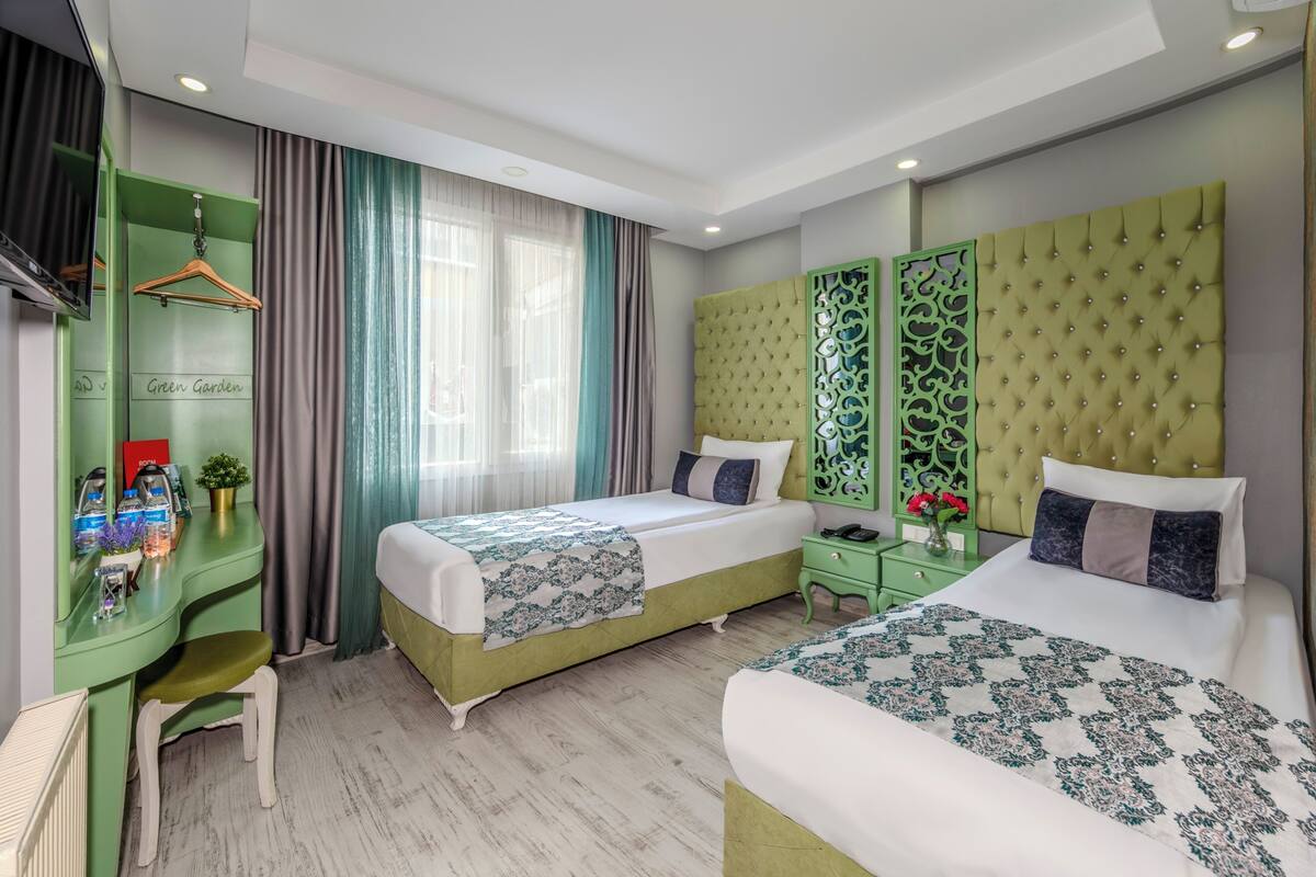 A hotel room with two beds, a desk, and a green wardrobe.