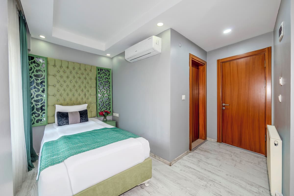A bedroom with a bed, green headboard, wooden door, and an air conditioning unit.