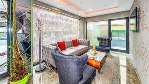 A modern living room with a sofa, armchairs, and a coffee table. There is a large window with curtains and a view of greenery outside. - Green Garden Hotel (Istanbul)