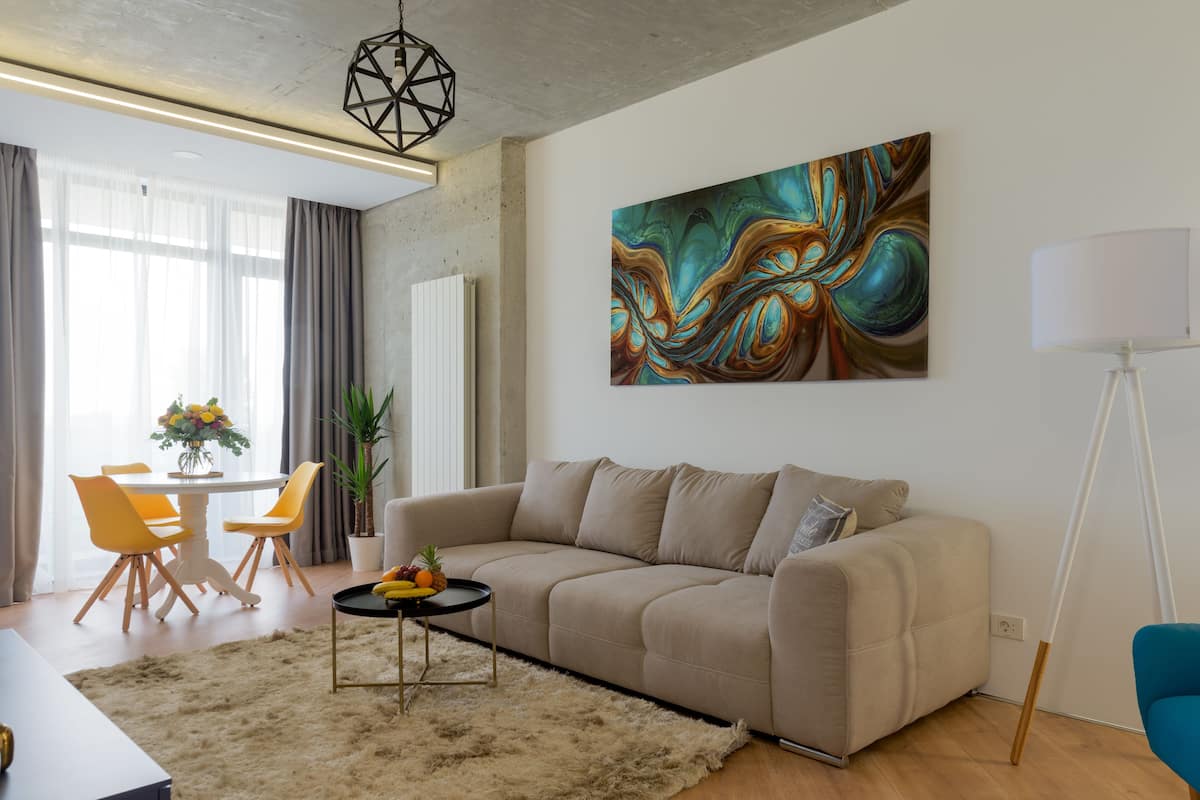 A modern living room with a beige sofa, a round coffee table, and a colorful abstract painting on the wall.