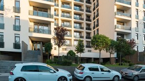 Un edificio residencial de varios pisos con balcones, zona de estacionamiento y entrada arbolada.