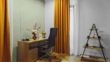 A room with a wooden desk, a black office chair, a globe, a vase with flowers, and a wooden shelf with decorative items.