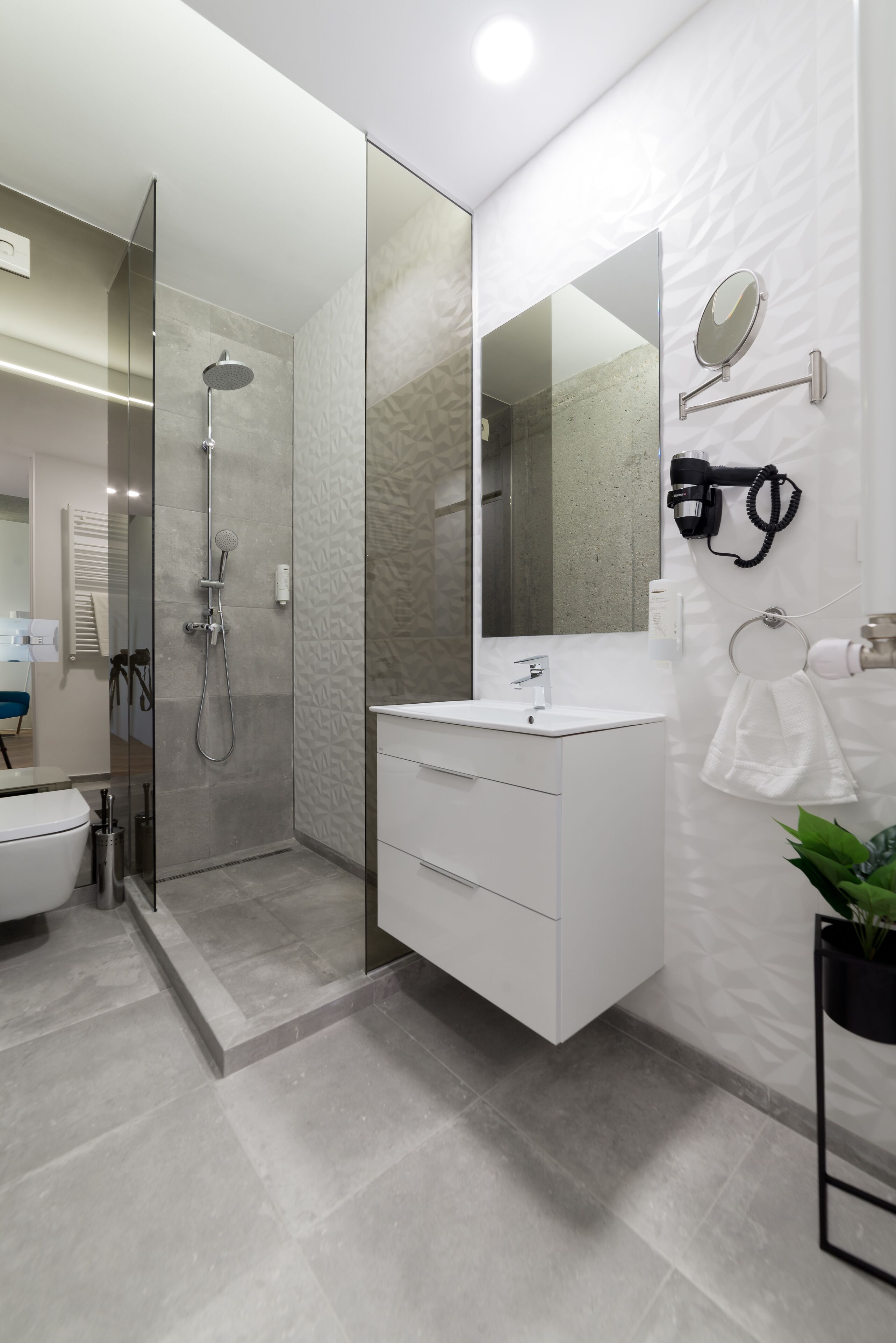 A modern bathroom with a glass-enclosed shower, a white vanity with a mirror, and a potted plant.
