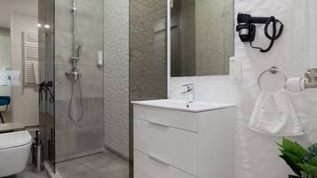 A modern bathroom with a glass-enclosed shower, a white vanity with a mirror, and a potted plant.