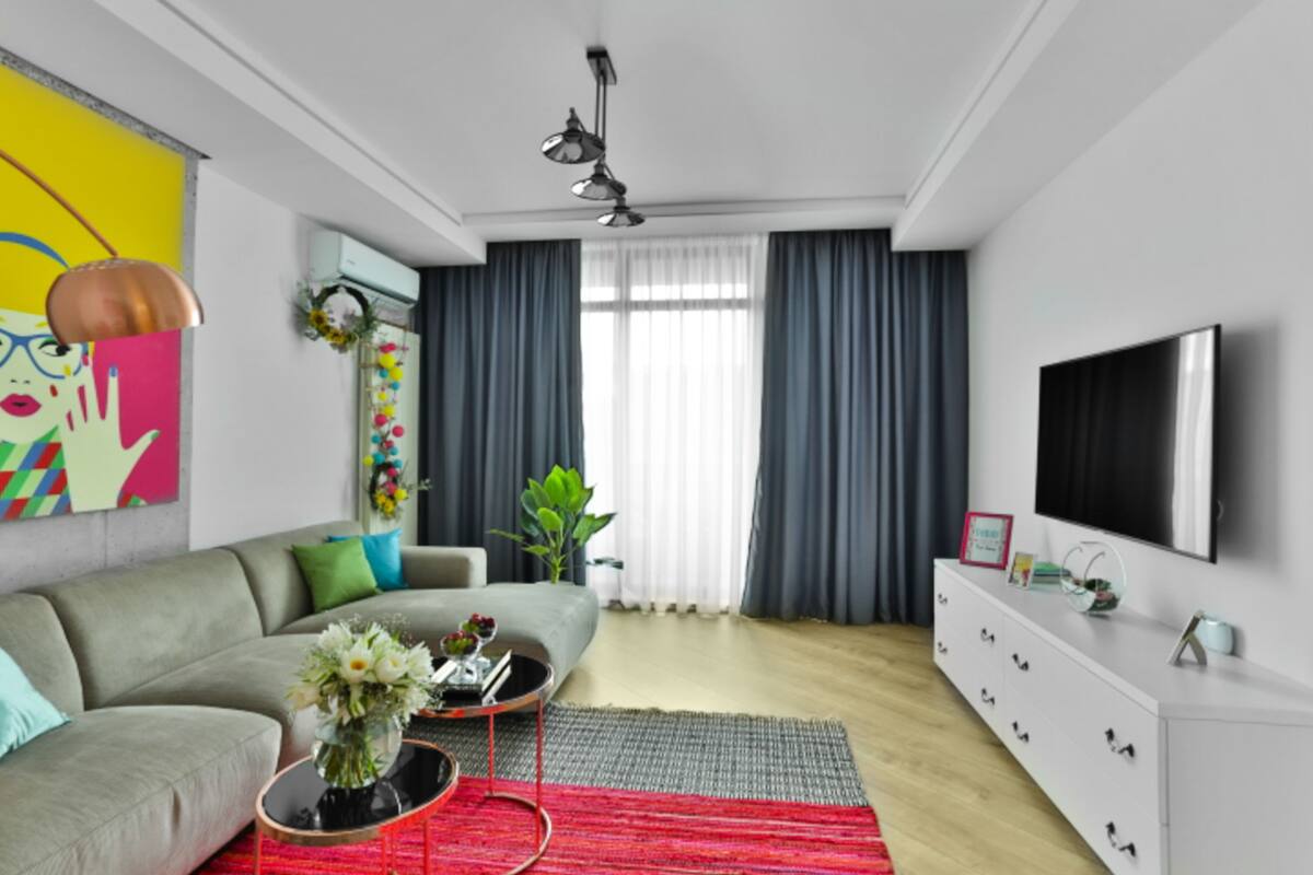 A modern living room with a grey sofa, a coffee table with a vase, a white dresser, and a flat-screen TV mounted on the wall.
