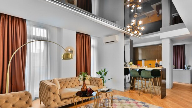 Una sala moderna con sofá, mesa de centro y alfombra estampada. Cuenta con una zona de cocina con taburetes de bar y una mesa de comedor.
