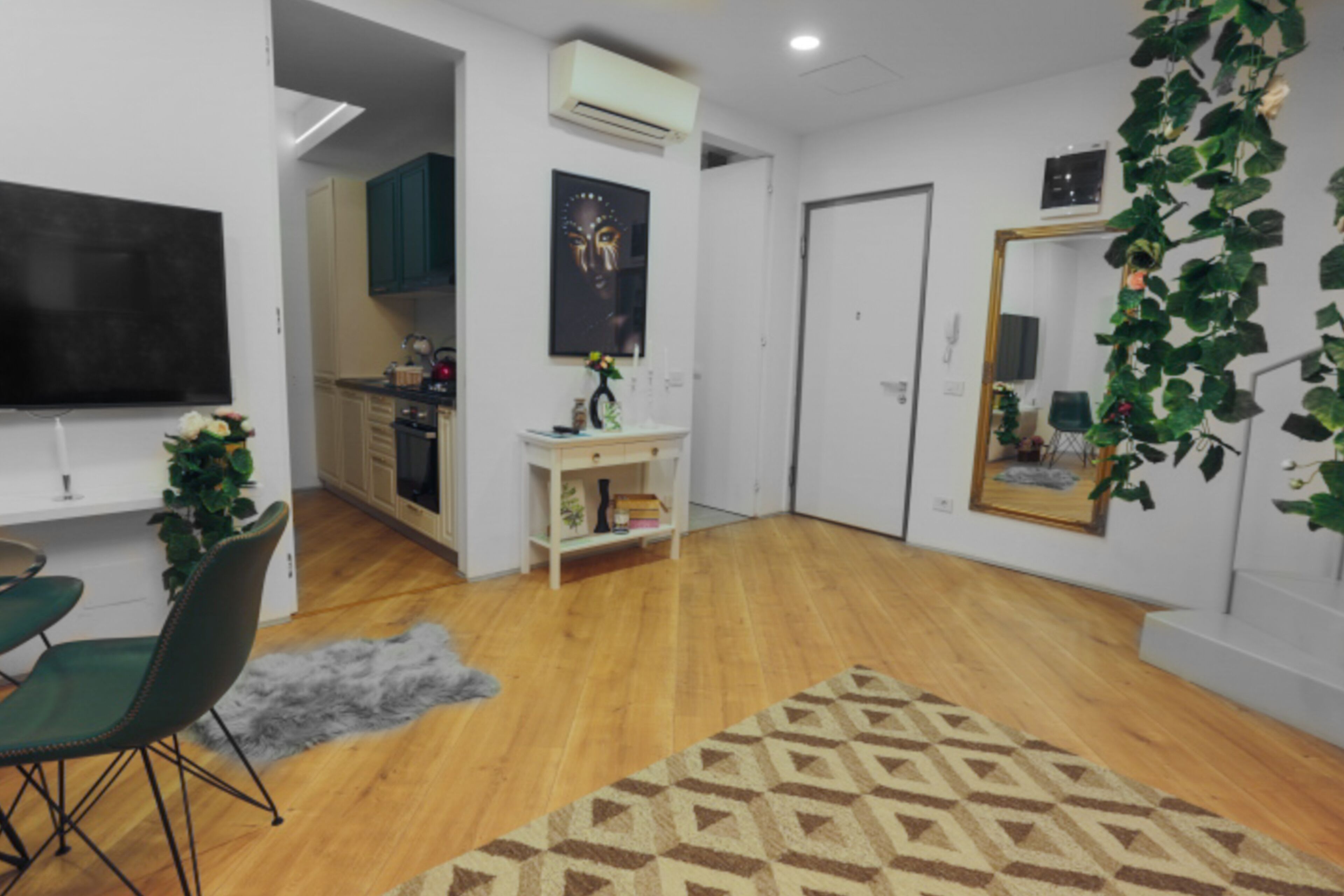 A modern living room with a wooden floor, a patterned rug, a green sofa, and a dining area with a table and chairs.