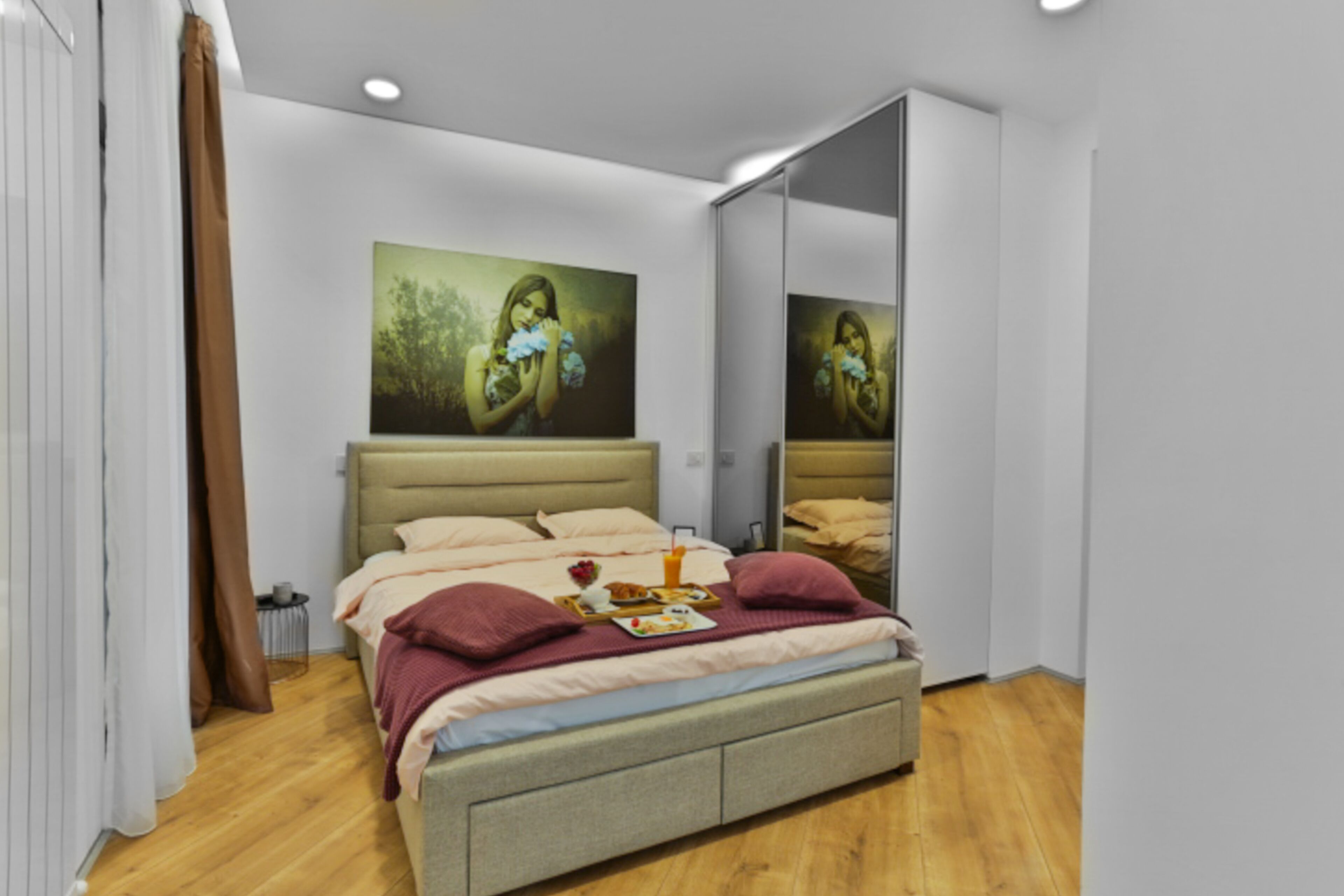 Une chambre à coucher moderne avec un lit, un tableau, un miroir et une table de chevet.