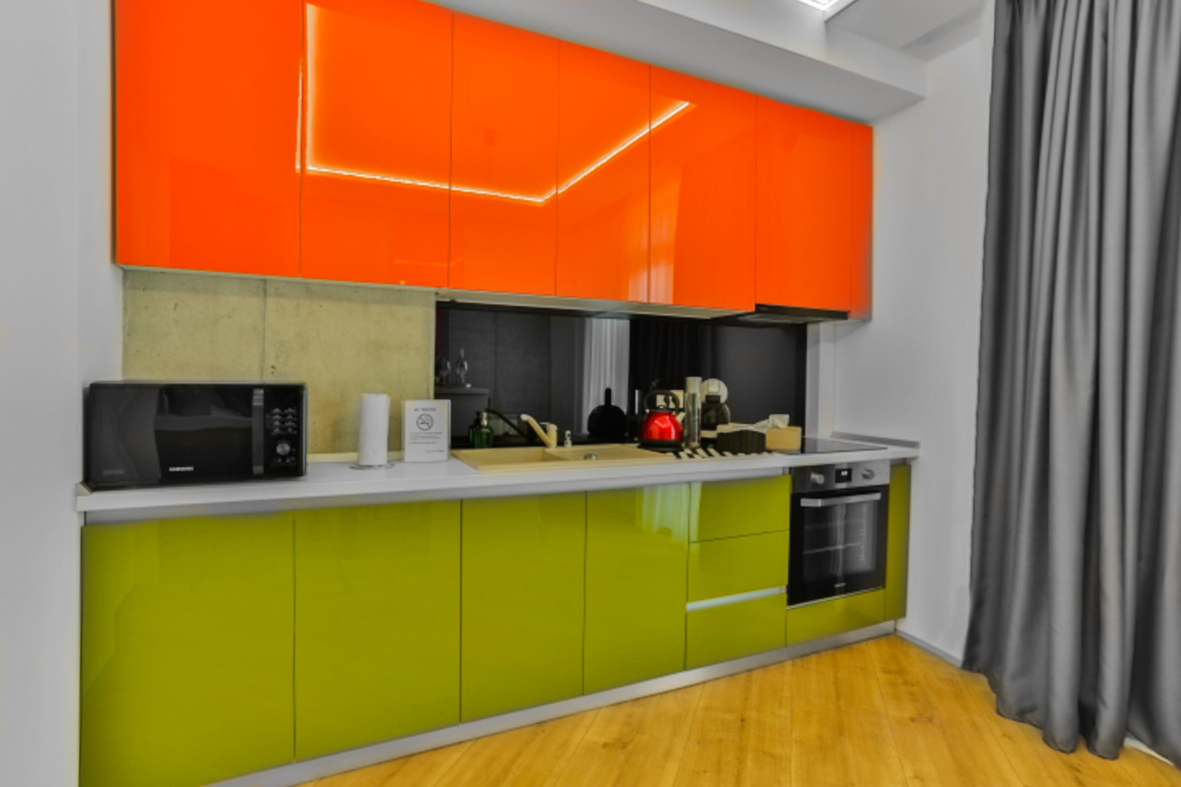 A modern kitchen with green and orange cabinets, a microwave, a kettle, and a dishwasher.