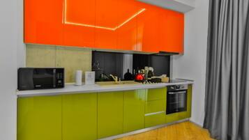A modern kitchen with green and orange cabinets, a microwave, a kettle, and a dishwasher.