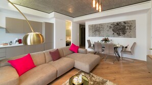 Una sala de estar moderna con un sofá modular, un comedor con mesa y sillas, y una cocina al fondo.