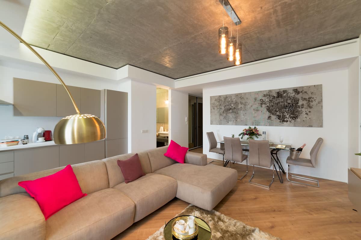 A modern living room with a sectional sofa, a dining area with a table and chairs, and a kitchen in the background.