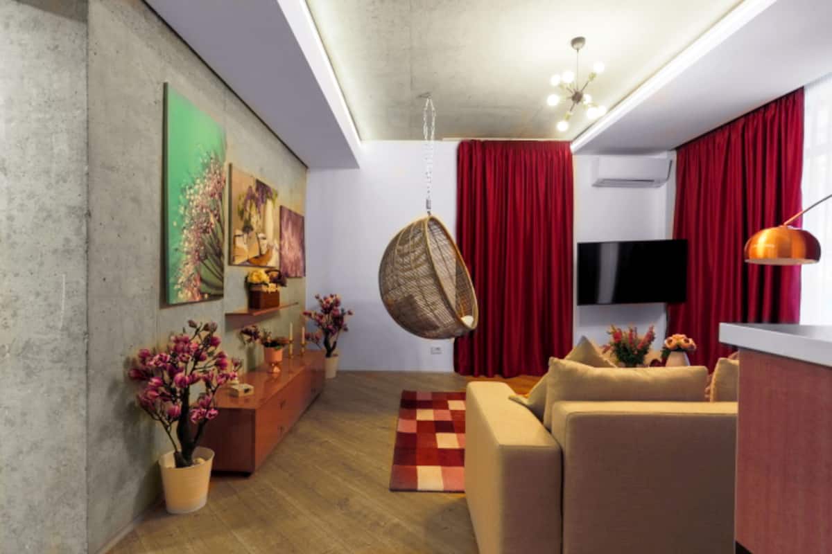 A modern living room with a sofa, a hanging chair, a flat-screen TV, and a red curtain.