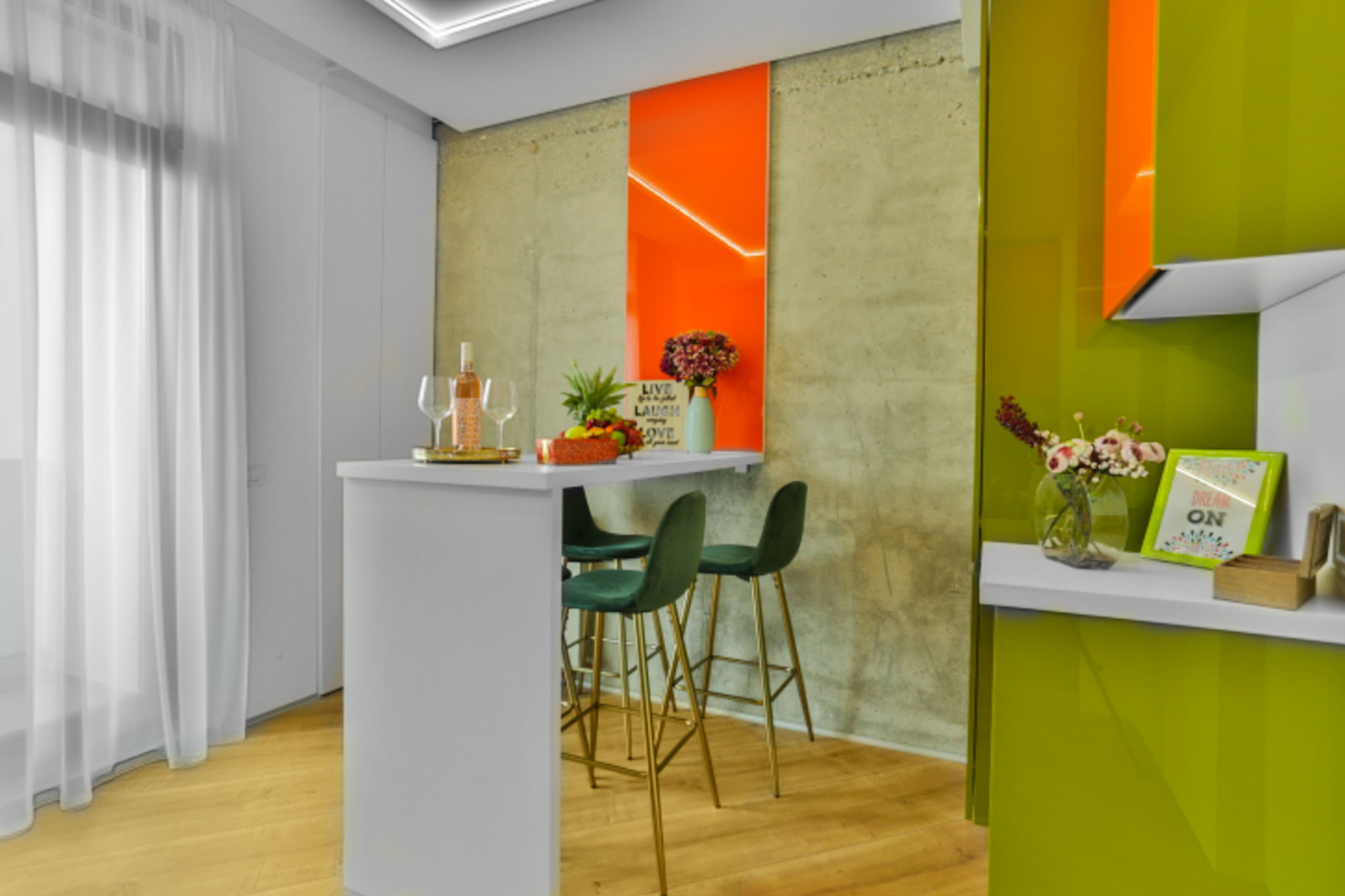 A modern bar area with a white counter, green chairs, and a vibrant orange accent wall.
