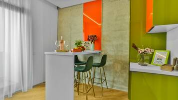 A modern bar area with a white counter, green chairs, and a vibrant orange accent wall.