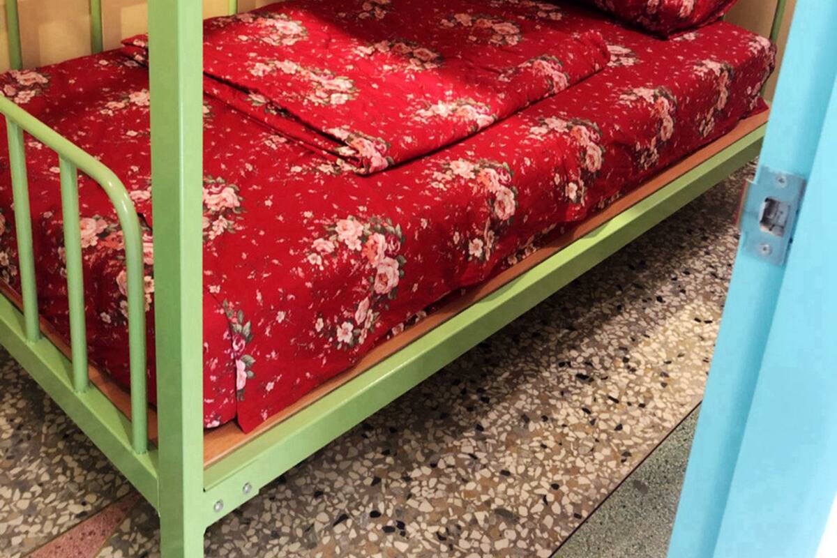Uma cama de solteiro com colcha florida, grades de metal e piso de azulejos.